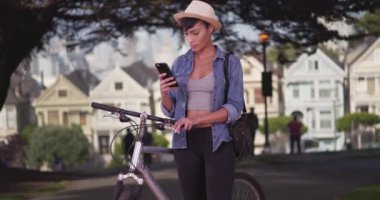 San Francisco Parkı 'nda bisiklete yaslanmış cep telefonuyla mesajlaşan güzel hippi kadın. Mutlu siyah kadın 20 'li yaşlarda..