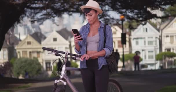 サンフランシスコ公園の携帯電話でメールしてるから自転車にもたれてるから 幸せな黒女性で彼女の20代 — ストック動画