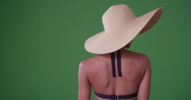 Güneş şapkalı genç bir Afro-Amerikalı kadın yeşil ekranda bikinisiyle kameradan kafasını çeviriyor. Anahtar ya da birleşik olmak üzere yeşil ekranda.