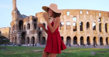 Colosseum 'un yanında kırmızı elbiseyle dans eden sevimli melez kadın. Tasasız milenyum kızı yazın Roma 'da eğleniyor, gülümsüyor ve gülüyor. 4k