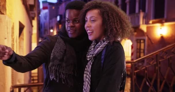 在威尼斯的桥上 一对可爱的千禧年夫妇站在桥上观看大运河 快乐迷人的黑人男性和女性在晚上观看贡多拉小船 — 图库视频影像