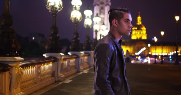 パリの美しい夜にポンアレクサンドル3世橋の上に立っているハンサムな100万人の男 レザージャケットのハンサムなラテン男性は夜に誰かを待っています — ストック動画