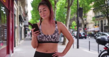 Asyalı bir kadın cep telefonuyla şehir mesajlarında koşuyor. Mutlu, gülümseyen bir kadın, akıllı telefondan sokak mesajlaşması. 4k