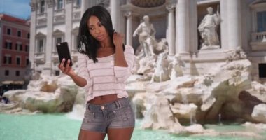 Roma, İtalya 'daki çekici Afrikalı kadın sosyal medyaya selfie çekiyor. Güzel siyah kadın Trevi Çeşmesi 'nin önünde kendi fotoğrafını çekiyor ve yüklüyor. 4k