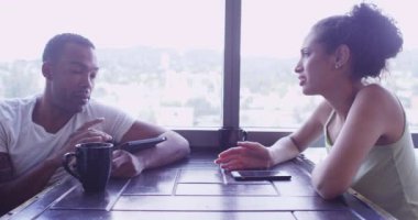 Latin ve Siyah çift oturma odasında akıllı telefon ve tablet bilgisayar kullanıyorlar.