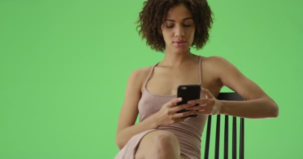 一个千年的非洲裔美国女孩随随便便摆姿势 在绿色的屏幕上看着她的手机 在绿色屏幕上键入或合成 — 图库视频影像
