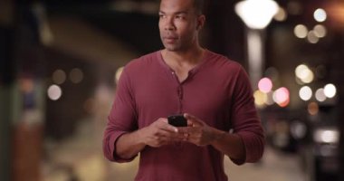 Siyahi bir adam şehir caddesinde cep telefonuyla mesaj atıyor. Afro-Amerikalı bir adam akıllı telefonunu metropolitan bölgesinde kullanıyor. 4k