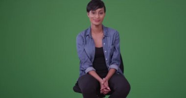 Genç bir Afro-Amerikalı kadının portresi. Ofis sandalyesinde kameraya gülümseyen yeşil ekranda kot gömlek giyen bir kadın. Anahtar ya da birleşik olmak üzere yeşil ekranda.