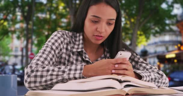 工作过度的西班牙裔女学生在电话里给同学发短信 讲述课堂上讨论的一个概念 紧张的拉丁大学生在她的智能手机书里看到了一个令人困惑的概念 — 图库视频影像