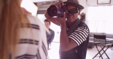 Siyah moda fotoğrafçısı, arkasında asistanlardan oluşan bir ekiple stüdyoda fotoğraf çekiyor.