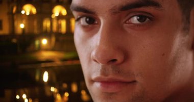 Geceleri dışarıda kameraya bakan 20 'li yaşlarda yakışıklı bir Latin adamın portresi. Akşamları dışarıda dikilen mutlu ve çekici turistleri kapatın. 4k