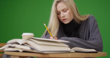 Yeşil ekranda dönem ödevi için okuyan ve yazan güzel bir genç kadın. Anahtar ya da birleşik olmak üzere yeşil ekranda.