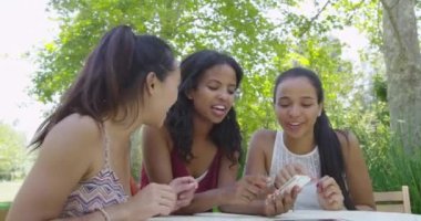 Kız arkadaşlar akıllı telefon kullanırken gülüp konuşuyorlar.