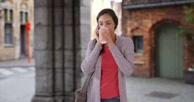 Tatlı İspanyol bayan kahve içiyor ve akıllı telefonda sohbet ediyor. Güzel Latin kadın cep telefonuyla konuşuyor, gülümsüyor ve gülüyor. 4k