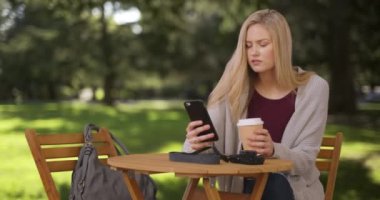 Sıradan bir genç kadın parkta oturmuş, mesajlaşıyor ve içiyor.