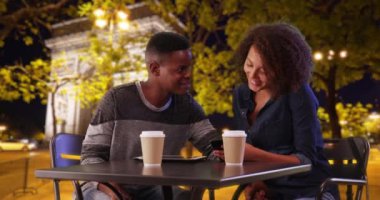 Siyah çift Paris 'te sohbet etmekten ve akıllı telefon kullanmaktan zevk alıyor. Mutlu Afrikalı Amerikalı erkek ve kadın gece Paris caddesinde kahve içerler. 4k