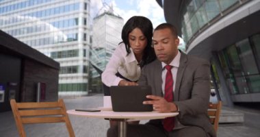 İki genç Afrikalı iş ortağı bir tablet cihazda sunum düzenliyor. Siyahi erkek ve kadın iş adamları iş bilgilerine bir defter üzerinden bakıyorlar. 4k