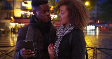 Yakışıklı siyah adam Paris caddesinde kız arkadaşıyla cep telefonu kullanıyor. Mutlu Afro-Amerikan erkek geceleri şehir caddesinde 4G cep telefonu kullanıyor. 4k