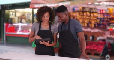Londra caddesindeki markette dijital tablet kullanan gülümseyen iki garson. Siyah erkek ve kadın yemek şirketi önlük takıyor kablosuz dokunmatik ekranda geziniyor. 4k
