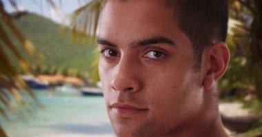 Millennial İspanyol turistin Karayip plaj tatilindeki portresi. Latin adam tropikal okyanus kıyısında kameraya bakıyor. 4k.