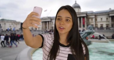 Trafalgar Meydanı 'nda sosyal medya hesabı için selfie çeken tatlı Latin bir kadın. Mutlu çekici milenyum turistleri Londra 'da kendi fotoğraflarını çekiyor. 4k