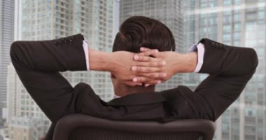 Ofis sandalyesine yaslanıp pencereden şehre bakan işadamlarının dikiz manzarası. Yüksek katlı, manzaralı genç bir iş adamı. 4k