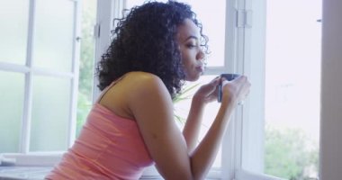 Afrikalı kadın elinde kupayla pencerede duruyor.