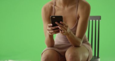 Gecelikli siyah bir kız yeşil ekranda akıllı telefonundan bakıyor. Anahtar ya da birleşik olmak üzere yeşil ekranda.