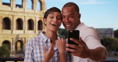 Yeni nişanlı Afrikalı erkek ve dişi Roma, İtalya 'da tatildeyken akıllı bir telefonla fotoğraf çekiyor. Coşkulu etnik çift Roma Kolezyumu yakınlarında nişanlanmaktan zevk alıyor. 4k