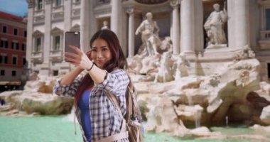 Trevi Çeşmesi 'nde selfie çeken mutlu çekici Japon kadın. Gülümseyen turist Roma 'da kendi fotoğrafını çekiyor. 4k