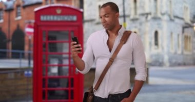 İngiltere 'de tatilde olan genç Afrikalı erkek akıllı telefonuyla arkadaşlarına mesaj atıyor. Yakışıklı siyahi adam cep telefonuyla Windsor, İngiltere 'nin fotoğraflarını gönderiyor. 4k