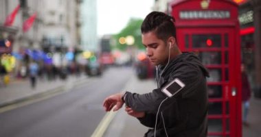 İspanyol milenyum erkek koşucusu koşuya ara verirken akıllı adımlar atıyor. Londra caddesindeki Latin koşucu müzik dinlerken spor takip cihazını kontrol ediyor. 4k