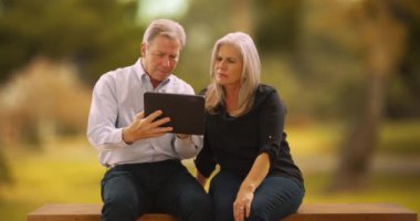 Tablet bilgisayar okuyan yakışıklı beyaz bir çift. Parkta tablet kullanan orta yaşlı bir çift..