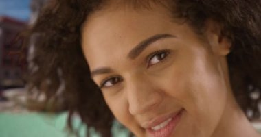 Çeşmenin yanındaki kameraya gülümseyen güzel, taze yüzlü Afrikalı kadının yakın çekimi. Kadının tatilde kamerayla gülümseyip güldüğü ve odak noktasından çıktığı yavaş çekim. 4k