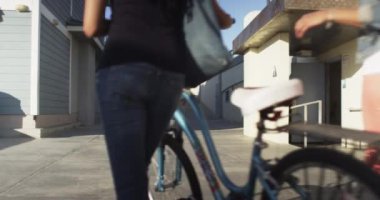 Güneşli bir günde, sahilde bisikletle yürüyen iki siyah kadın arkadaş.