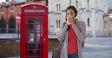 Güzel Latin kadın sohbetleri ve Windsor 'da sokakta kahve içmek. İngiltere 'de seyahat eden gülümseyen İspanyol kadın cep telefonundan arkadaşıyla konuşuyor, gülümsüyor ve gülüyor. 4k