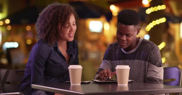 年轻的黑人男女晚上在城里喝咖啡 千年非洲裔美国人夫妇在平板电脑和智能手机上喝一杯 — 图库视频影像