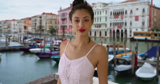 グランドキャナルに立って白いサンドレスで美しいラティーナの女性の肖像画 ヴェネツィアの休日にヒスパニック系の女性が喜んでカメラで笑顔 — ストック動画