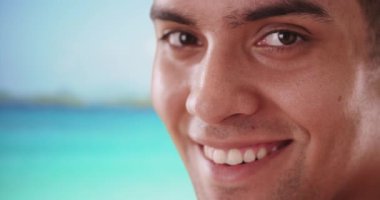 Okyanusun kıyısındaki mutlu, gülümseyen İspanyol Milenyum Turisti 'ne yaklaş. Tropikal tatilde olan Latin adam yüzünde gülümsemeyle kameraya bakıyor. 4k