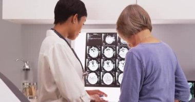 Afrikalı kadın doktor yaşlı bir hastayla röntgen taramalarını inceliyor.