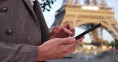 Paris 'te tatilde çektiği fotoğraflara bakarken beyaz bir kadının ellerinin yakın çekimleri. Eyfel Kulesi 'nin yanındaki cep telefonu cihazını kullanan genç bir kadın. 4k