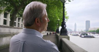 Londra 'daki olgun beyaz adam Thames nehrinin kenarına bakıyor. Tatilde olan yaşlı bir erkek Thames nehrinin kıyısına bakarken kendi kendine düşünür. 4k