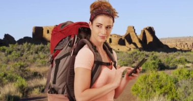 Genç bayan yürüyüşçü çöldeki yol haritasına bakmak için akıllı telefon kullanıyor. 20 'li yaşlarda akıllı telefon kullanan bir kadının yan görüntüsü