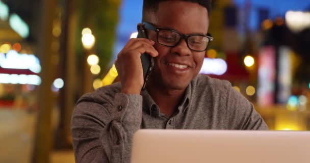 ハッピーミレニアルオフィスワーカーは シャンゼリゼ通りの電話でチャットします アフリカ系アメリカ人の男性は夜電話でノートパソコンの話をしている — ストック動画