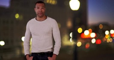 Yakışıklı siyahi adam gülümsüyor ve geceleri caddede dikiliyor. 20 'li yaşlarda Afro-Amerikan bir adam. 4k.