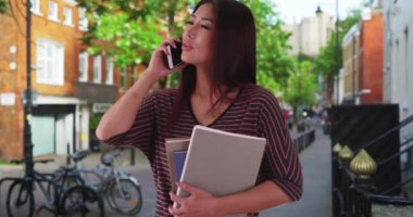 Yurt dışında okuyan güzel bir Asyalı kadın cep telefonuyla sohbet ediyor. Üniversite öğrencisi arkadaşlarıyla telefonda konuşurken gülümsüyor ve gülüyor. 4k