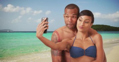 Siyahi bir çift birbirlerine sarılıp sahilde selfie çekiyorlar. Afrika kökenli Amerikalı bir erkek ve kadın kıyıda fotoğraf çekiyorlar. 4k