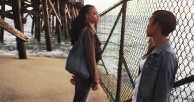 İskelenin altında dikilen siyah kadın cep telefonuyla gün batımının fotoğrafını çekiyor.