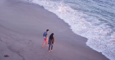 İki siyahi kadının sörf yaparken ayaklarını ıslattığı yüksek açılı bir manzara.