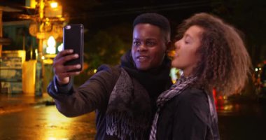Genç siyahi erkek ve kadın gece dışarıda selfie için poz veriyorlar. Milenyum Afrikalı Amerikalı çift şehirde fotoğraf çekiyor. 4k.